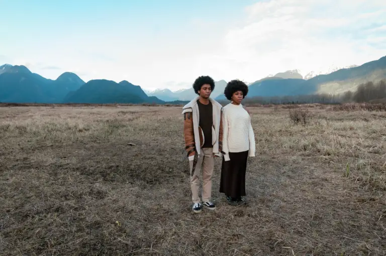 Two anxious individuals in a field surrounded by mountains