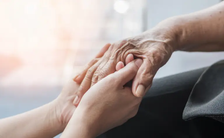 Older person with Alzheimer's holding the hand of their caregiver